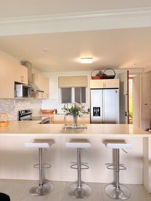 A modern kitchen with a central island, stainless steel appliances, and a view into the adjacent dining area. - The Snapdragon Courtyard Garden (Montego Bay)