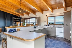 Een moderne keuken met een groot kookeiland, houten balkenplafond, uitzicht op zee en een boekenkast.