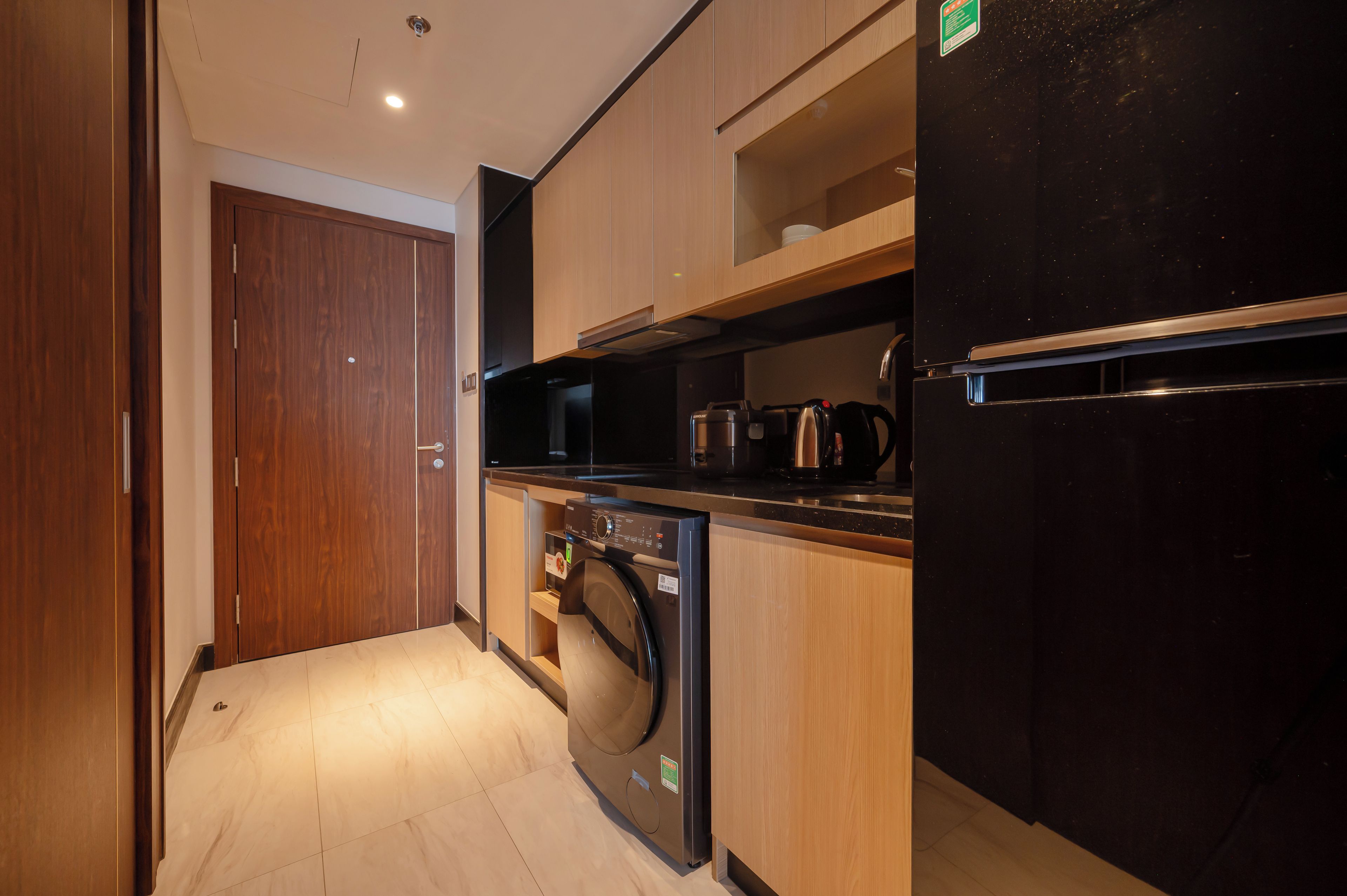 A compact kitchen with a washing machine, a black refrigerator, and wooden cabinets.