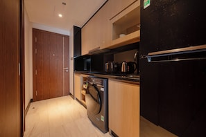 A compact kitchen with a washing machine, a black refrigerator, and wooden cabinets. - C Suite Soleil Da Nang - Free airport pick-up (An Hai)