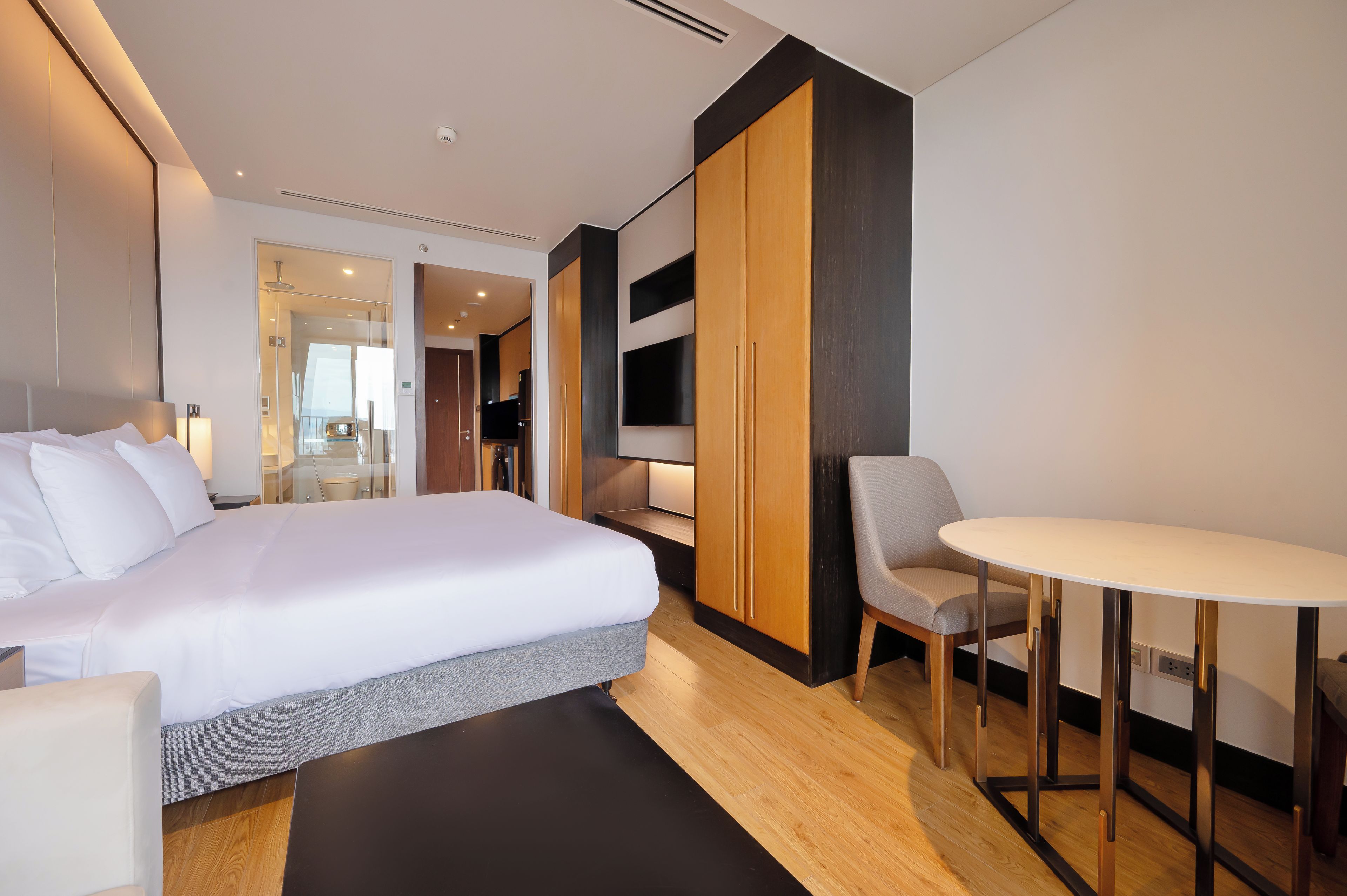 A modern hotel room with a large bed, a desk, a chair, and a TV.