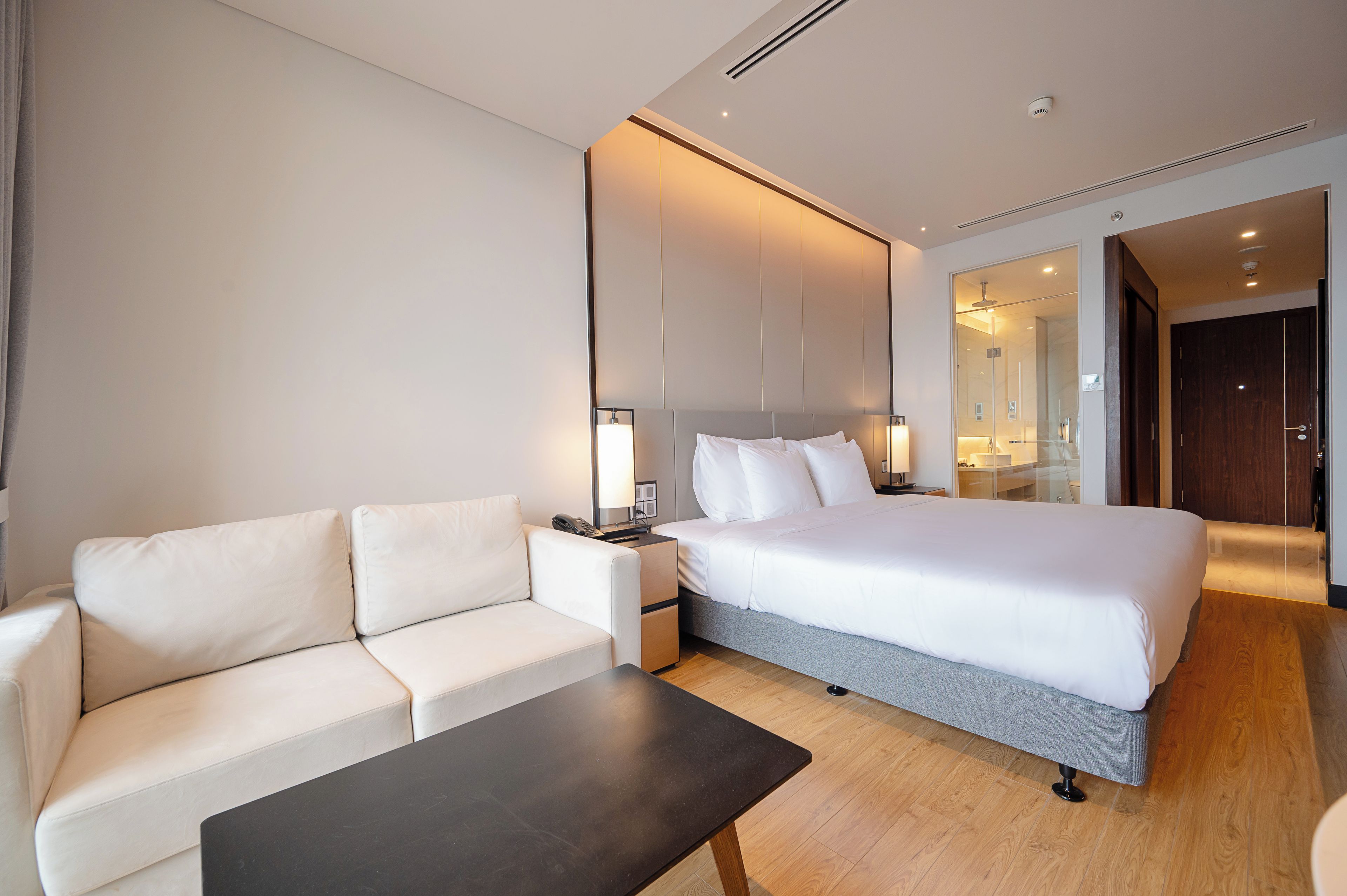 A hotel room with a bed, a sofa, a bedside table, and a mirror.