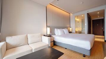 A hotel room with a bed, a sofa, a bedside table, and a mirror.