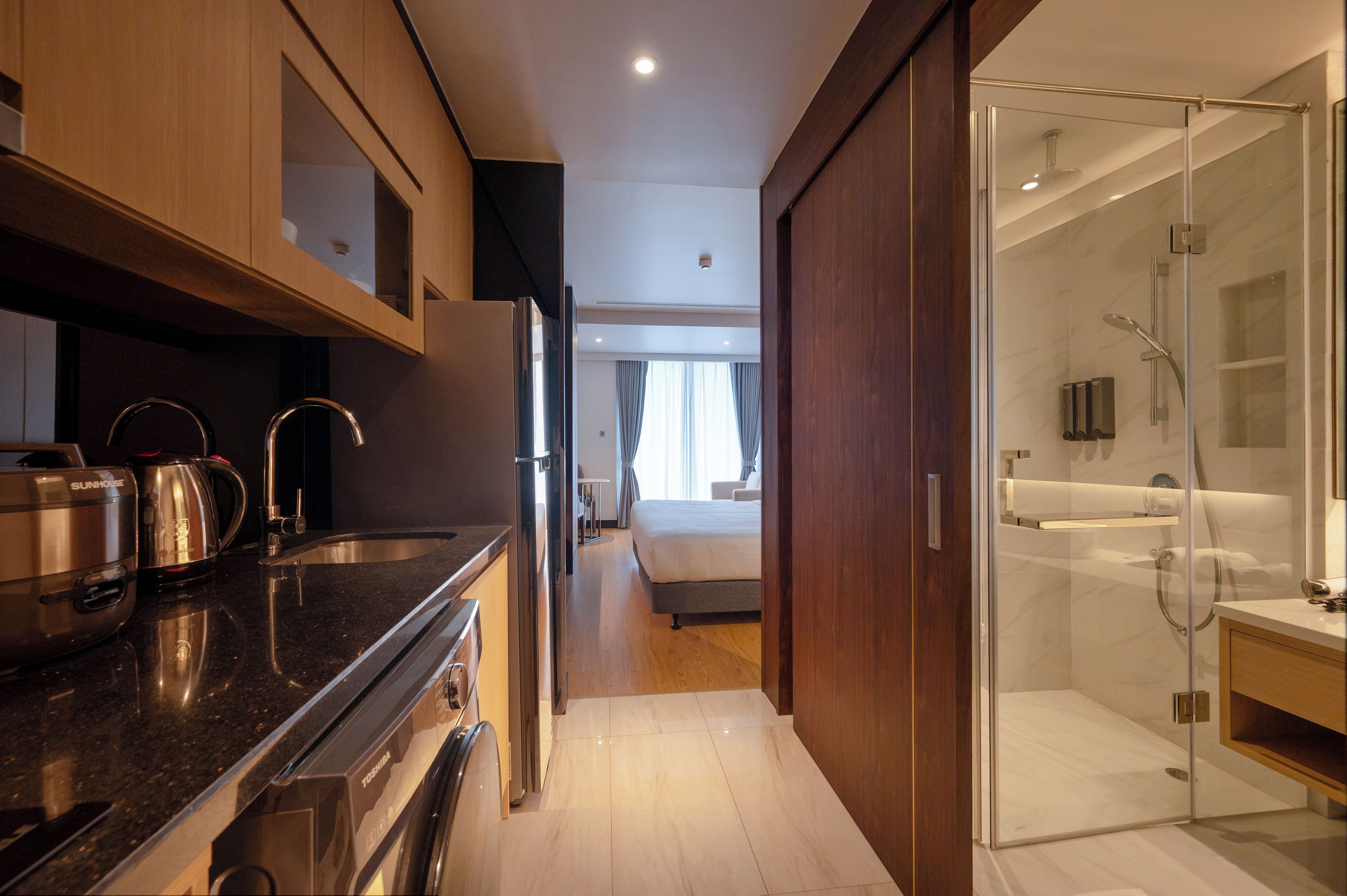 A hotel room with a kitchenette, a walk-in closet, and a glass-enclosed shower area.