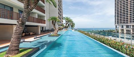 A swimming pool with a view of the ocean, surrounded by palm trees and modern buildings.