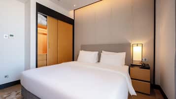 A hotel room with a large bed, a bedside table with a lamp, a wardrobe, and a thermostat on the wall.