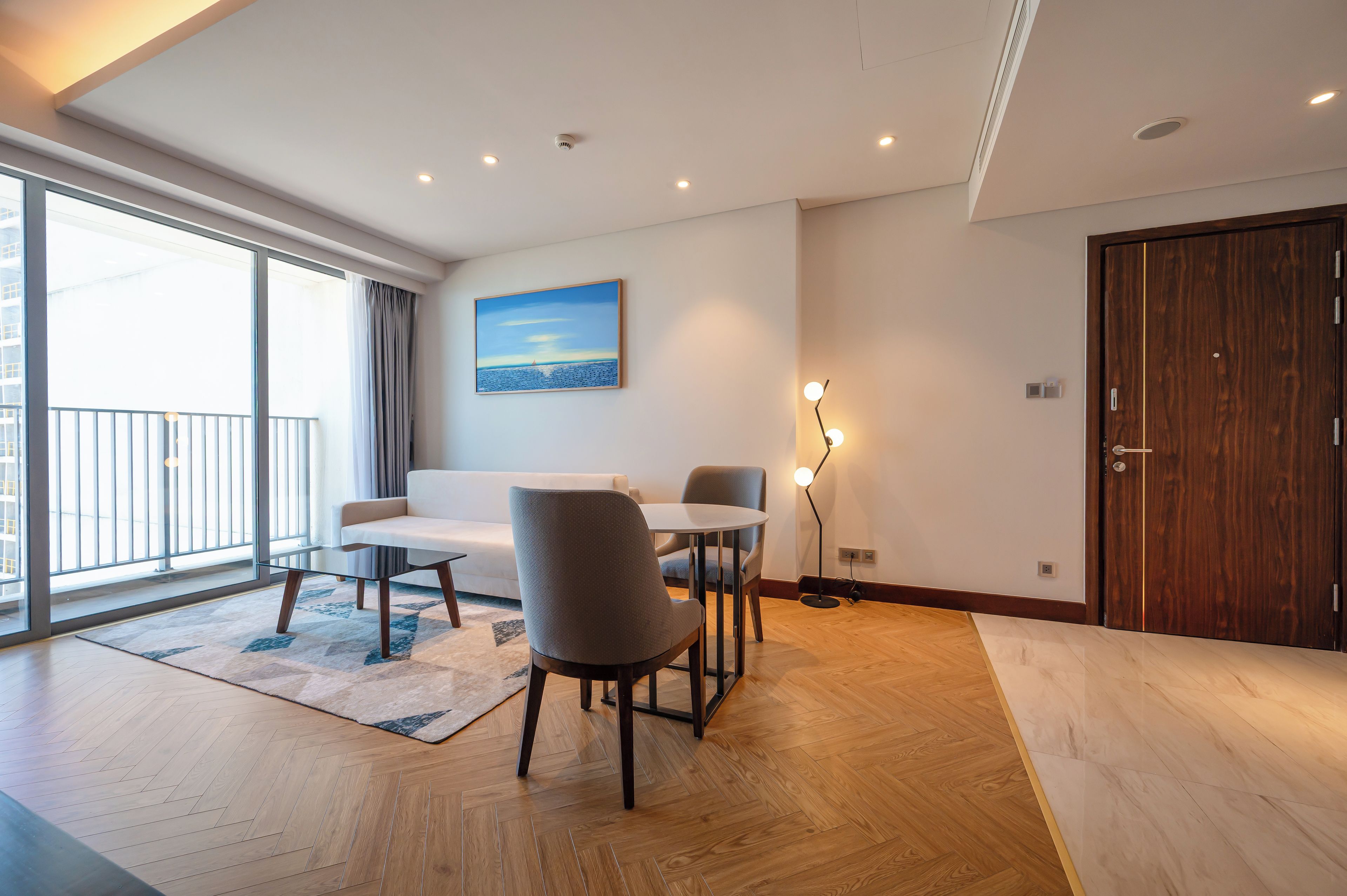 A modern living room with a sofa, chairs, a table, and a painting on the wall.
