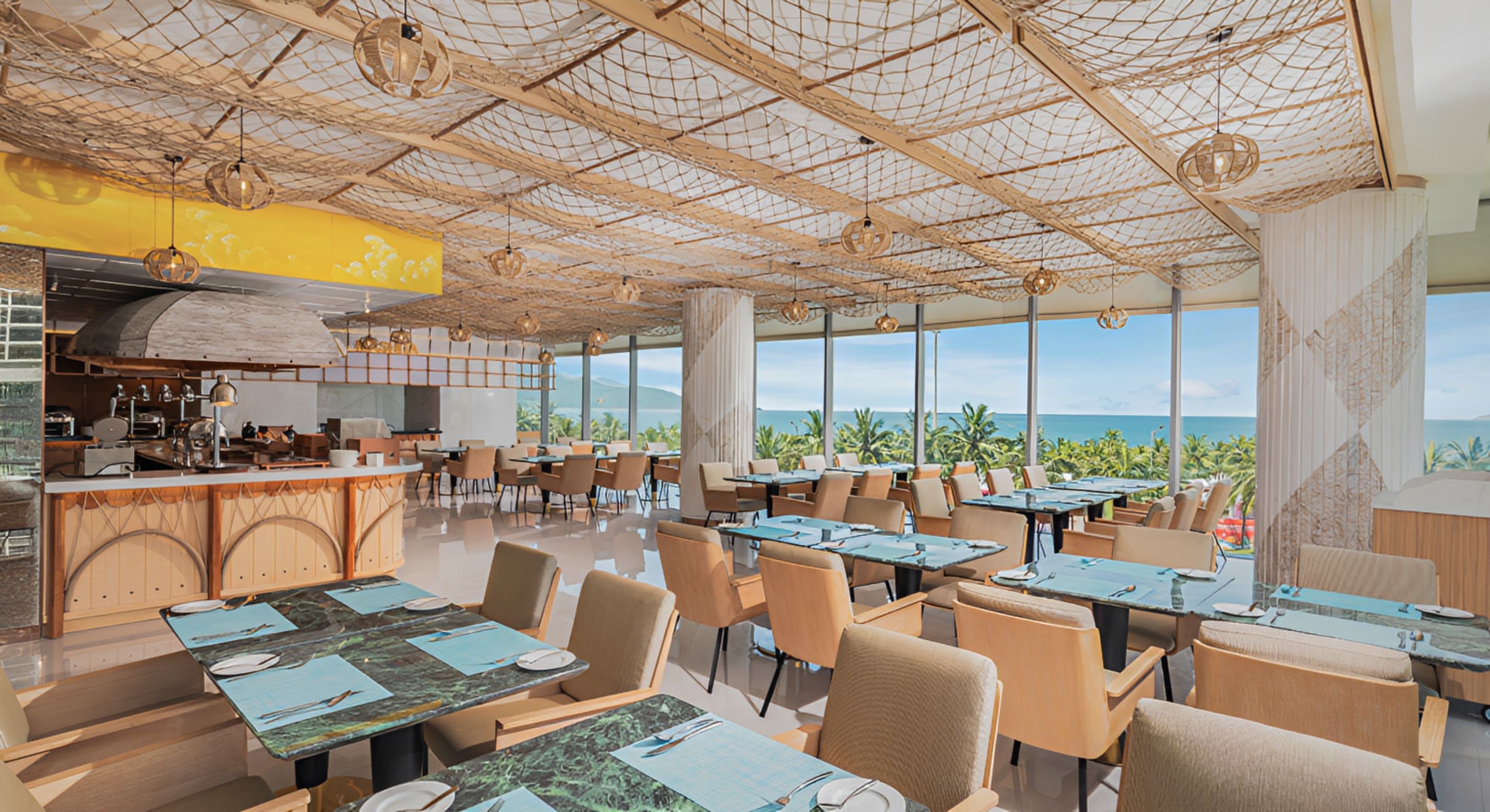 Een restaurant met uitzicht op de oceaan, met een hoog plafond en een netstructuur, houten tafels en stoelen.