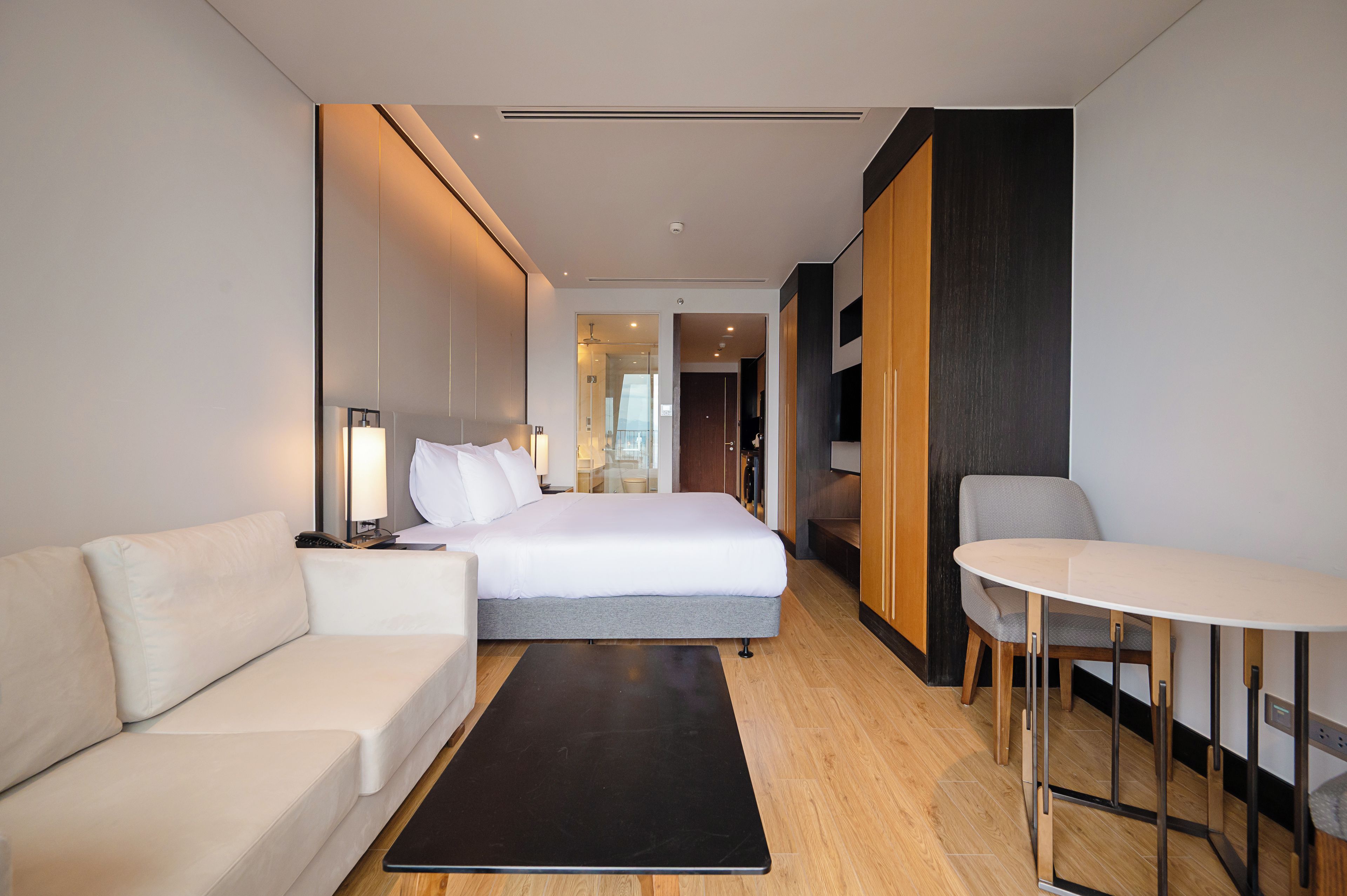 A modern hotel room with a bed, a sofa, a dining table, and a walk-in closet.