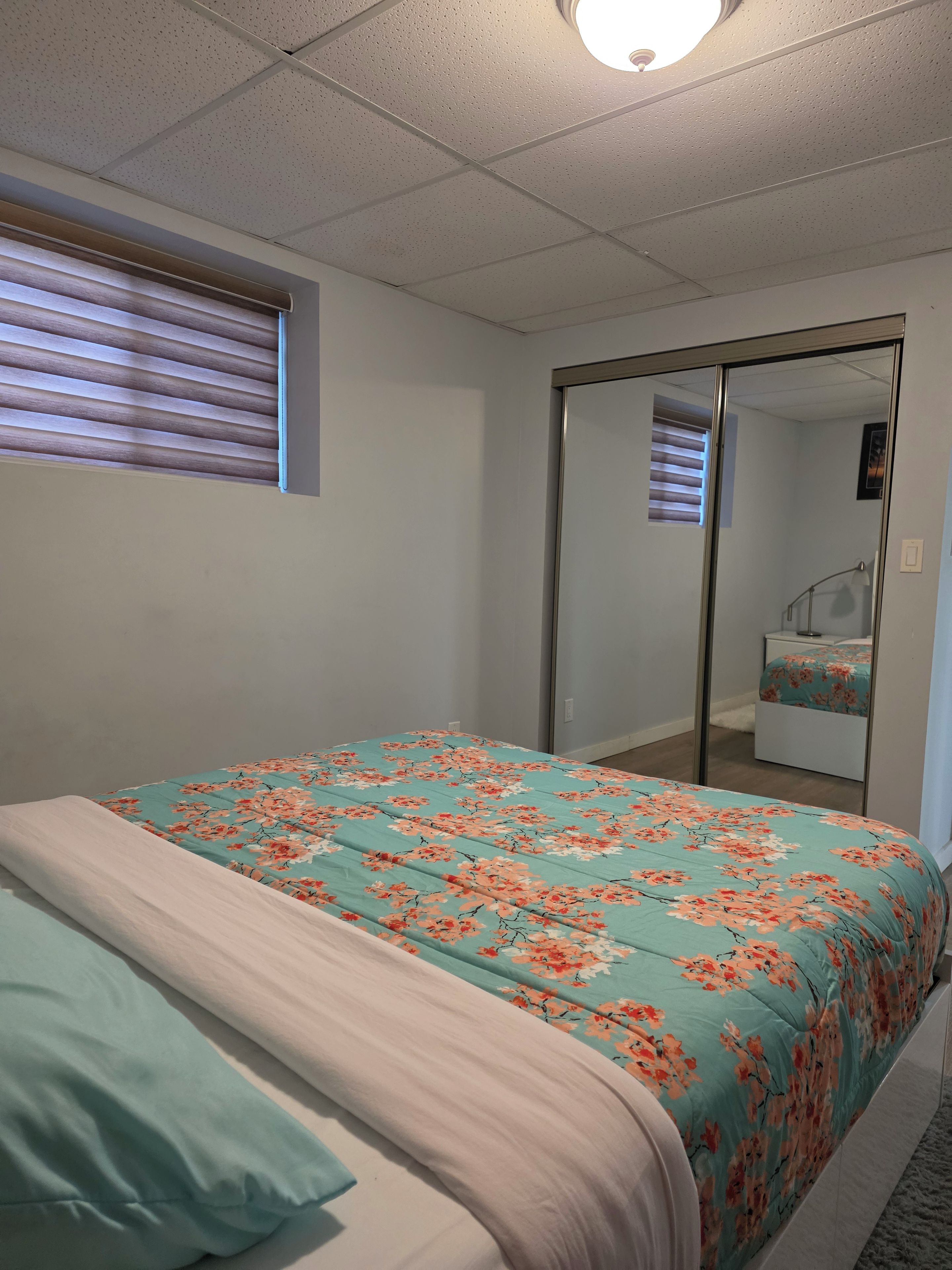A bedroom with a bed, a window with blinds, a sliding door, and a mirror.