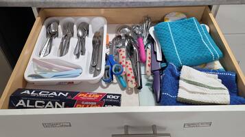 A kitchen drawer with utensils, a box of aluminum foil, and a dish rack.