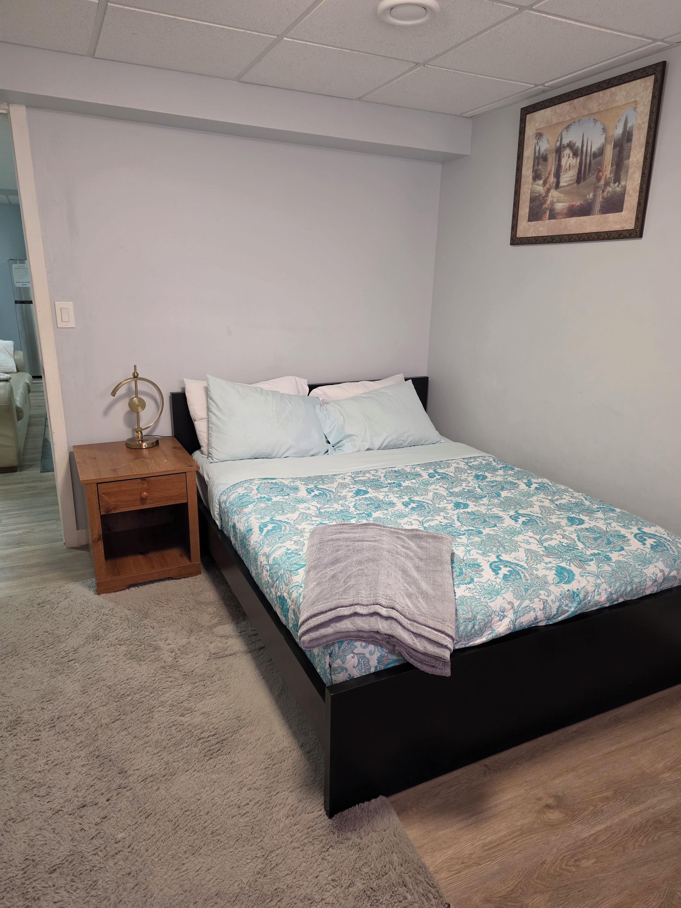 Une chambre à coucher avec un lit, une table de chevet, une lampe et un tableau au mur.