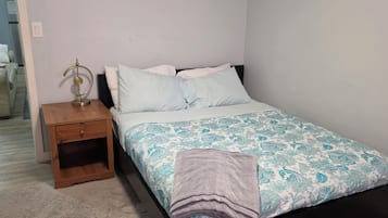 Een slaapkamer met een bed, een nachtkastje, een lamp en een schilderij aan de muur.