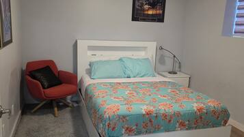 A bedroom with a bed, a red chair, a nightstand, a lamp, and a framed picture on the wall.
