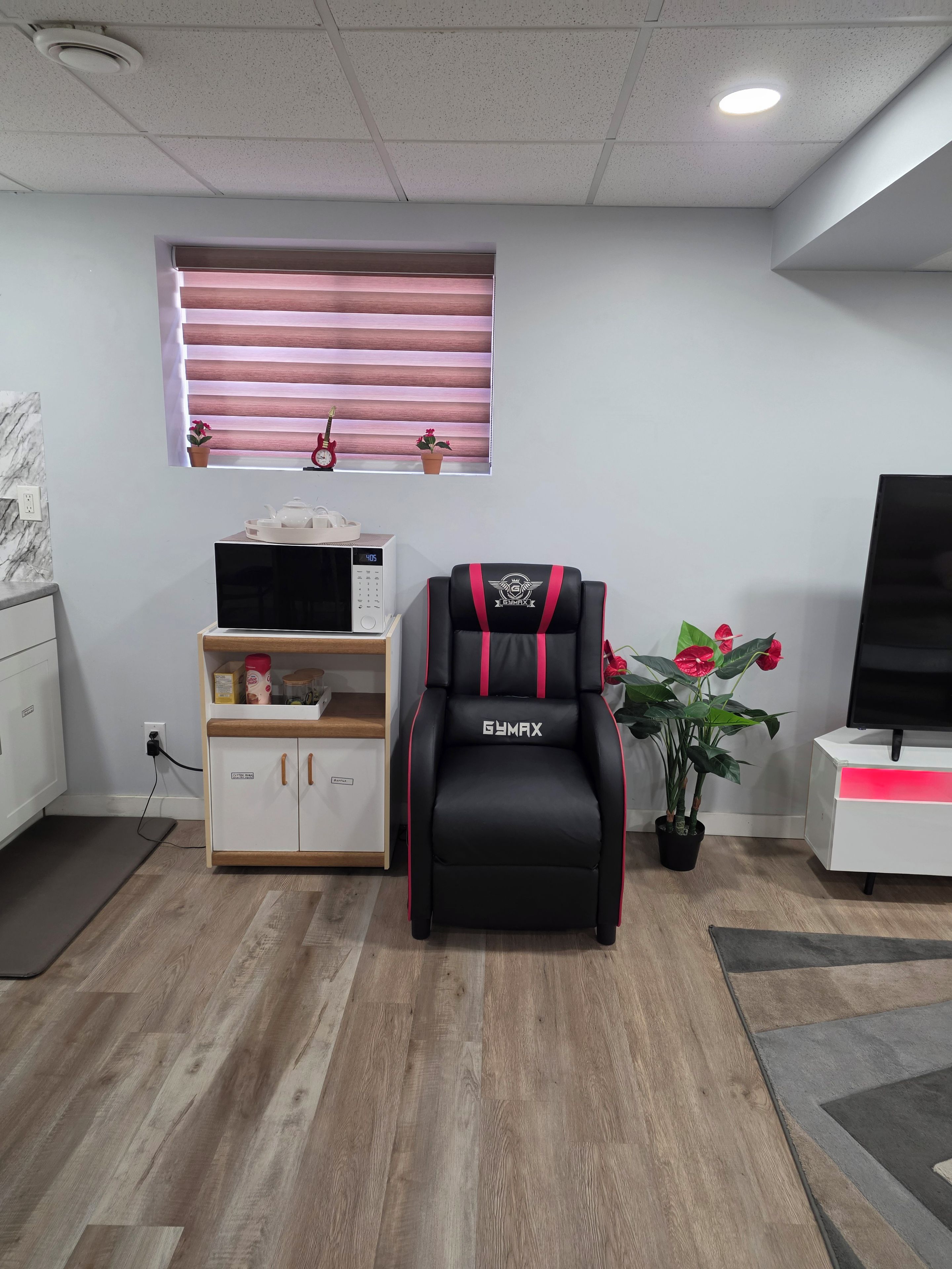 A modern living room with a black and red gym chair, a microwave, a small cabinet, a potted plant, and a television.
