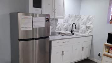 A modern kitchen with a stainless steel refrigerator, white cabinets, a marble backsplash, and a built-in sink.