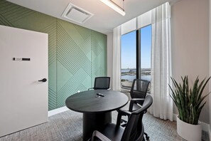 A conference room with a round table, two chairs, a potted plant, and a view of a body of water through large windows. - 501 First Corner Balcony by Palermo Home (Miami)