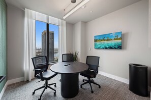 A modern conference room with a panoramic city view, a round table, two office chairs, a mounted television, and a trash bin. - 501 First Corner Balcony by Palermo Home (Miami)