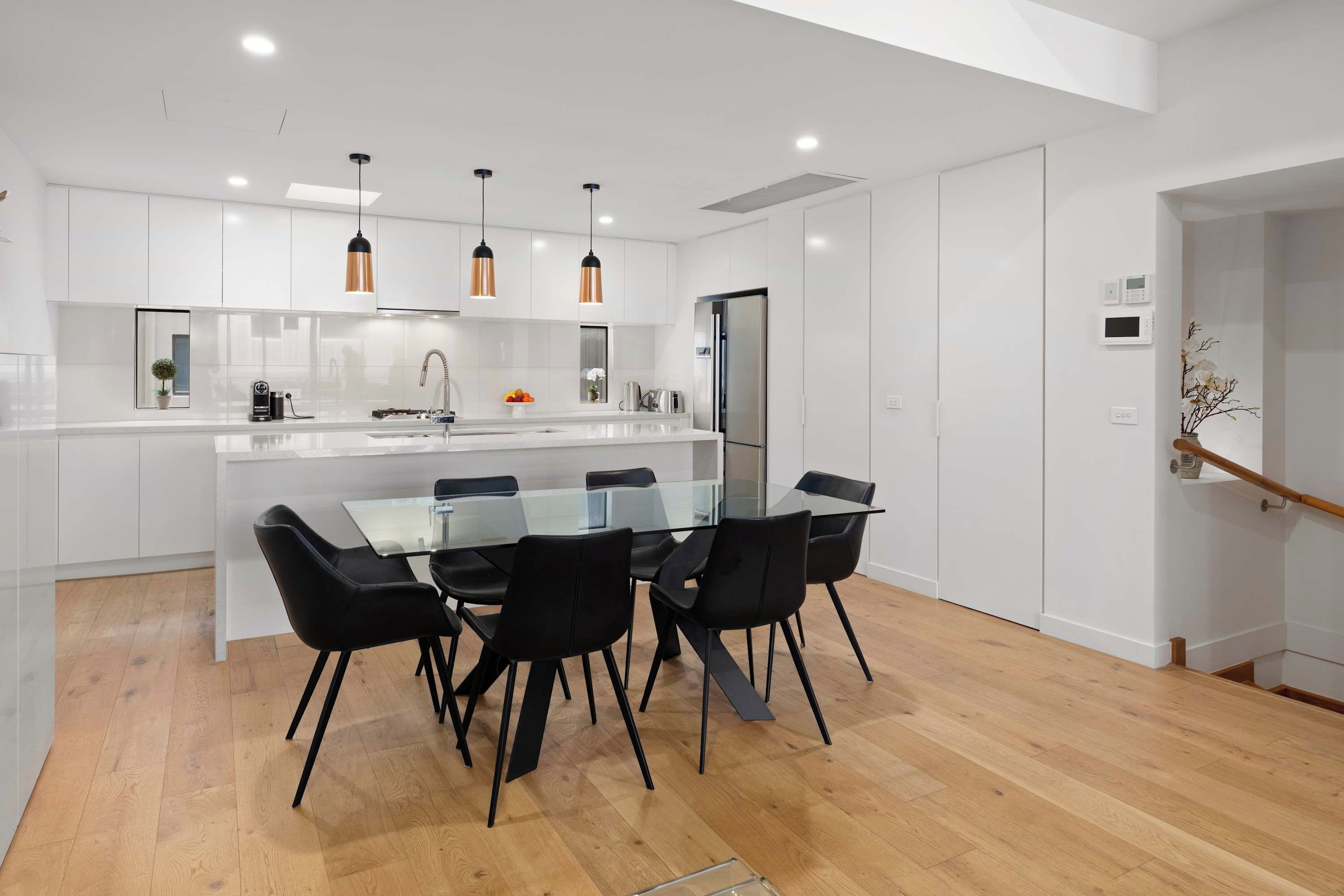 A modern kitchen with white cabinets, a glass dining table, and black chairs.