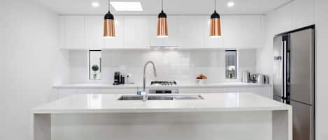 Una cocina moderna con una isla central, electrodomésticos de acero inoxidable e iluminación colgante.