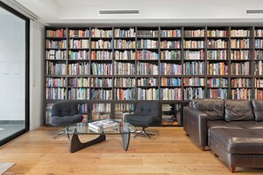 Ein modernes Wohnzimmer mit einer großen Bücherwand, zwei Sesseln, einem Glastisch und einem Ledersofa.