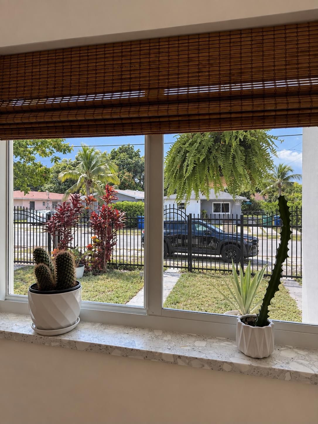 Ein Fenster mit Blick auf eine Straße, einen Zaun und ein geparktes Auto.