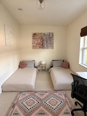 A room with two beds, a desk, a chair, a rug, and a painting on the wall.