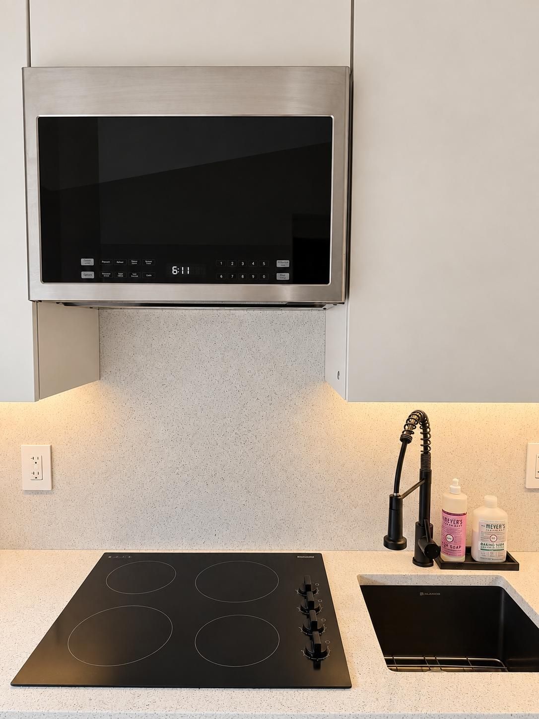 A kitchen with a stainless steel range hood, a black induction cooktop, and a sink with a faucet.