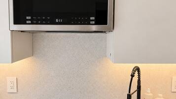 A kitchen with a stainless steel range hood, a black induction cooktop, and a sink with a faucet.