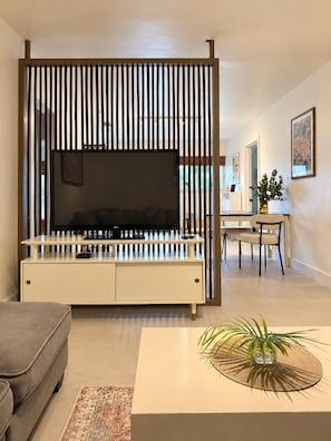 A modern living room with a flat-screen TV, a sofa, a coffee table, and a decorative plant.