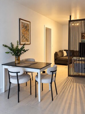 Een eethoek met een tafel, stoelen en een plant. Achtergrond is een bank en een scheidingswand.