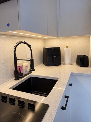 Een moderne keuken met een zwarte spoelbak, een koffieapparaat en een broodrooster.