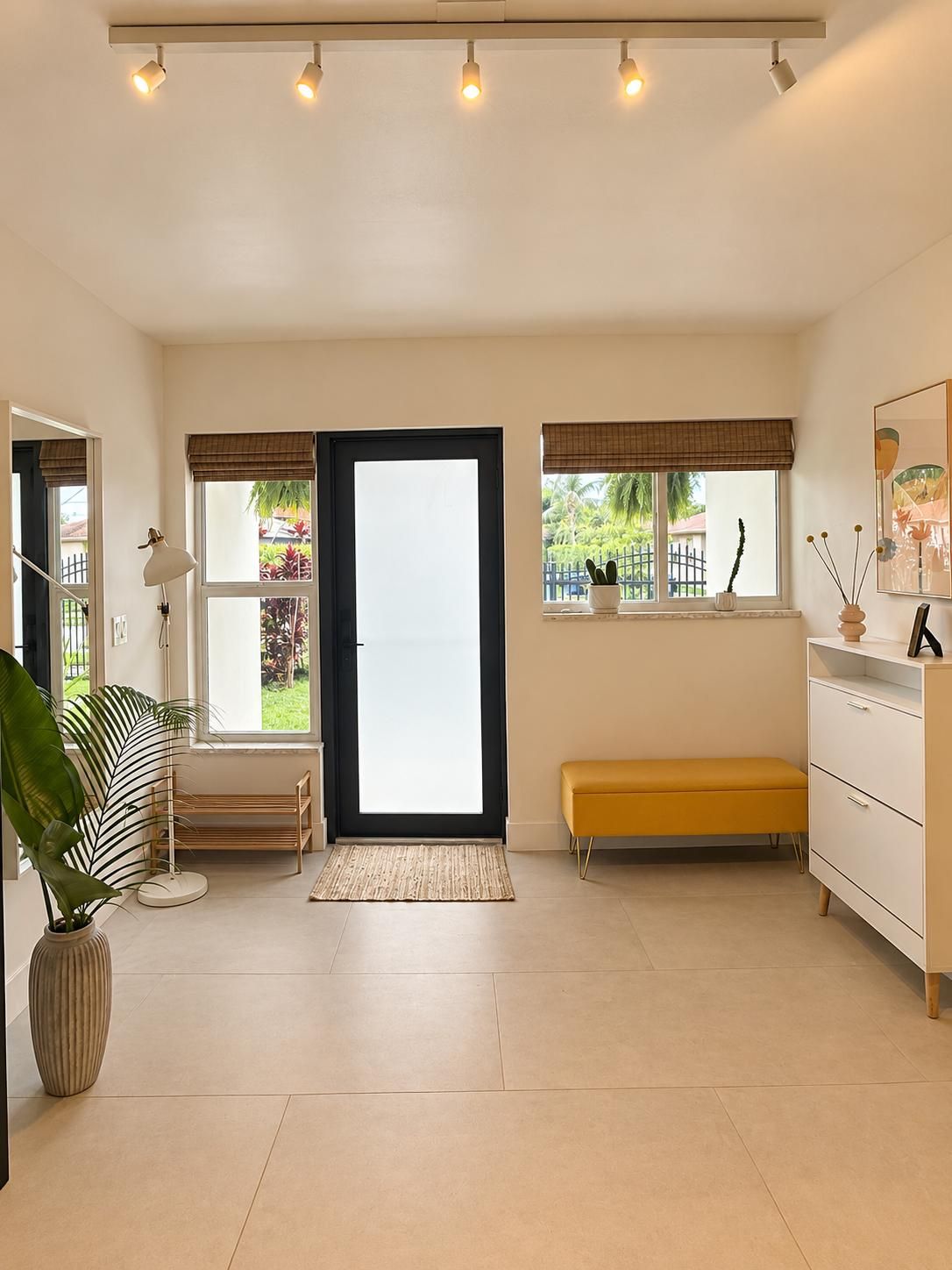 A spacious room with a large sliding door, a bench, a white dresser, and a potted plant.