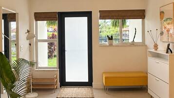 A spacious room with a large sliding door, a bench, a white dresser, and a potted plant.