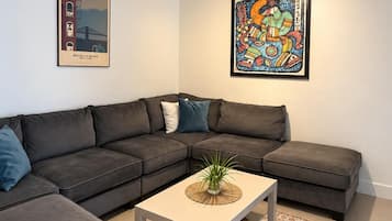 Ein modernes Wohnzimmer mit einem Ecksofa, einem Couchtisch und zwei gerahmten Kunstwerken an den Wänden.