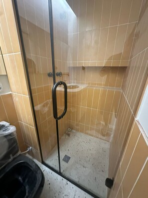 A shower with a glass door, beige tiles, and a black showerhead. - Swimming pool on the rooftop studio, 3 minutes from República Metro station. (São Paulo)