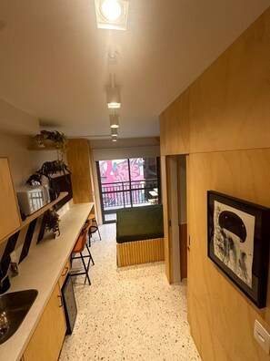 A compact kitchen with a built-in sink, a small dining area, and a view through a glass door to an outdoor balcony. - Swimming pool on the rooftop studio, 3 minutes from República Metro station. (São Paulo)