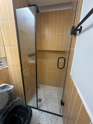 A small, enclosed shower area with a glass door, tiled walls, and a white door frame. - Swimming pool on the rooftop studio, 3 minutes from República Metro station. (São Paulo)