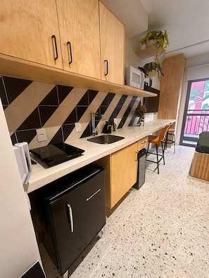 A kitchen with wooden cabinets, a black refrigerator, a microwave, and a sink. - Swimming pool on the rooftop studio, 3 minutes from República Metro station. (São Paulo)