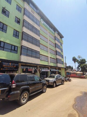 A multi-story building with a sign for a hotel. There are parked cars in front. - Hotel Delite (Chuka)