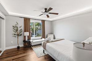 A bedroom with a bed, a bedside table, a lamp, a window with curtains, a ceiling fan, and a potted plant. - The Nutmeg Grand 4BR downtown San Diego retreat with patio, fire pit, WiFi & parking (San Diego)