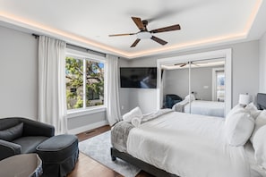 Ein modernes Hotelzimmer mit einem großen Bett, einem Deckenventilator, einem Flachbildfernseher und Blick auf Grün.
