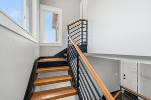 Een trap met houten treden en zwarte metalen leuningen, die uitkomt op een vloer met een witte deur.