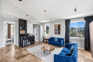 Ein modernes Wohnzimmer mit einem blauen Sofa, einem Couchtisch und einer Küchenzeile mit Mikrowelle und Kaffeemaschine.