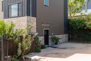 Een modern huis met twee verdiepingen, een gevel van natuursteen, een houten hek en verschillende planten.