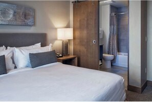Ein Hotelzimmer mit Bett, Nachttisch, Lampe und Blick ins Badezimmer.