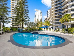 A swimming pool surrounded by lounge chairs and palm trees, with high-rise buildings in the background. - Contemporary Lvl17 2B2B Apt with Ocean Views (Gold Coast)