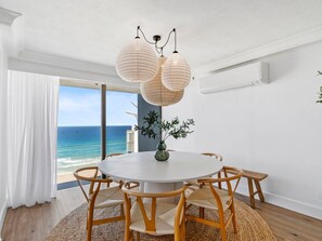 A round dining table with chairs, a vase with greenery, and a view of the ocean through a large window. - Contemporary Lvl17 2B2B Apt with Ocean Views (Gold Coast)