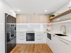 A modern kitchen with white cabinetry, a stainless steel refrigerator, a built-in oven, and a sink with a gold faucet. - Contemporary Lvl17 2B2B Apt with Ocean Views (Gold Coast)