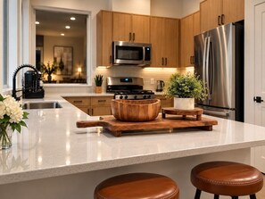 A modern kitchen with wooden cabinets, stainless steel appliances, a marble countertop, and a central island with stools. - Regent Sol - Scandinavian Luxury - Central Austin (Austin)